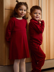 Two children in red outfits standing against a wooden wall.